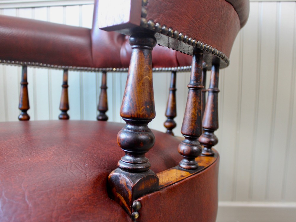 A Victorian oak elbow chair featuring deep buttoned reddish-brown leather upholstery, turned spindles, metal stud trim, and turned front legs. View VII