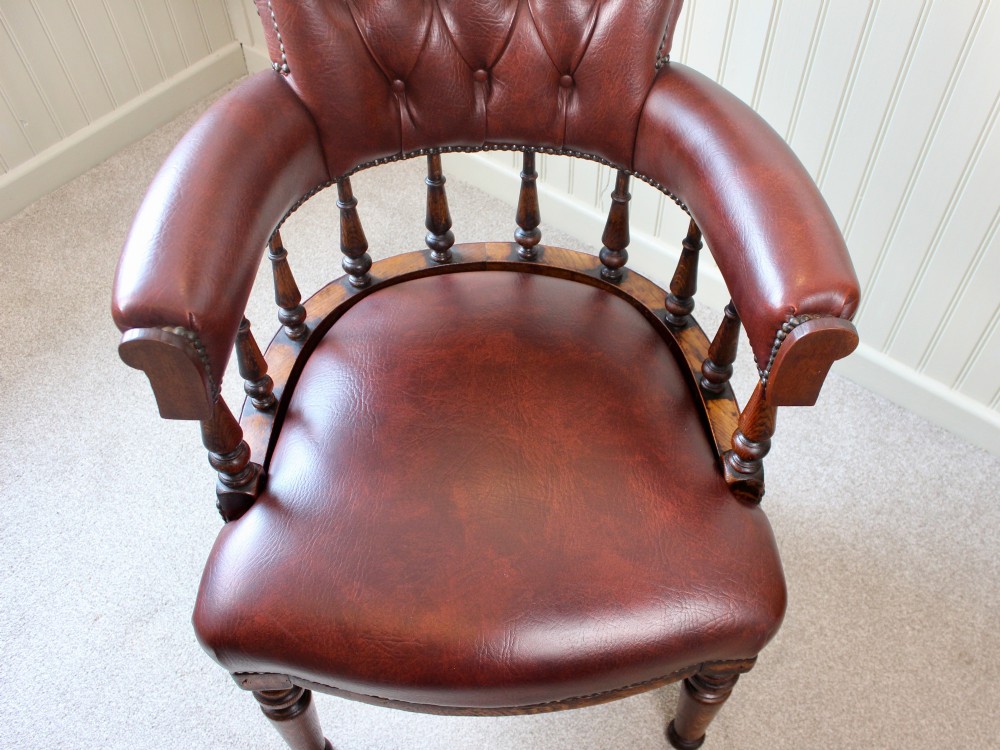A Victorian oak elbow chair featuring deep buttoned reddish-brown leather upholstery, turned spindles, metal stud trim, and turned front legs. View X