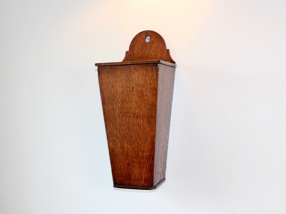 A George III tapered wall-hanging candle box crafted from warm brown oak with an arched crest panel and a top lid.