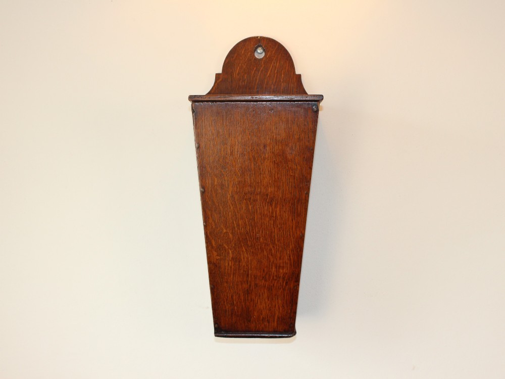 A George III tapered wall-hanging candle box crafted from warm brown oak with an arched crest panel and a top lid. View II