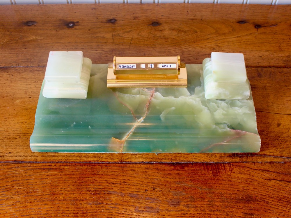 An Art Deco green onyx desk stand featuring a central gilt brass perpetual calendar flanked by two lidded onyx inkwells on a stepped rectangular base with a pen groove. View II