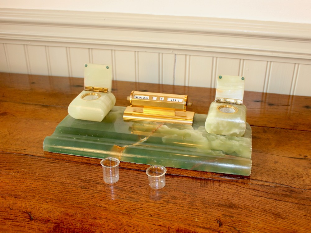 An Art Deco green onyx desk stand featuring a central gilt brass perpetual calendar flanked by two lidded onyx inkwells on a stepped rectangular base with a pen groove. View V