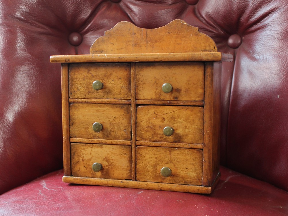 A small 19th-century fruitwood spice chest featuring six individual drawers with small brass knobs and a shaped back gallery.