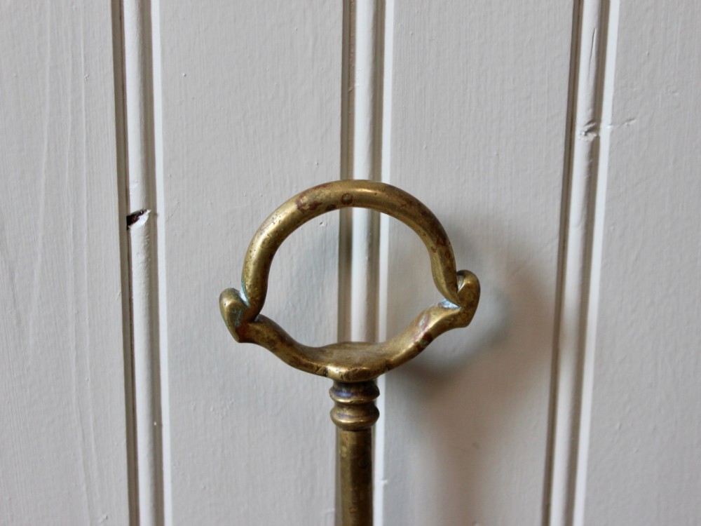 An antique Victorian cast brass door porter featuring a top loop handle, vertical stem, and weighted stepped base decorated with relief scrollwork. View II