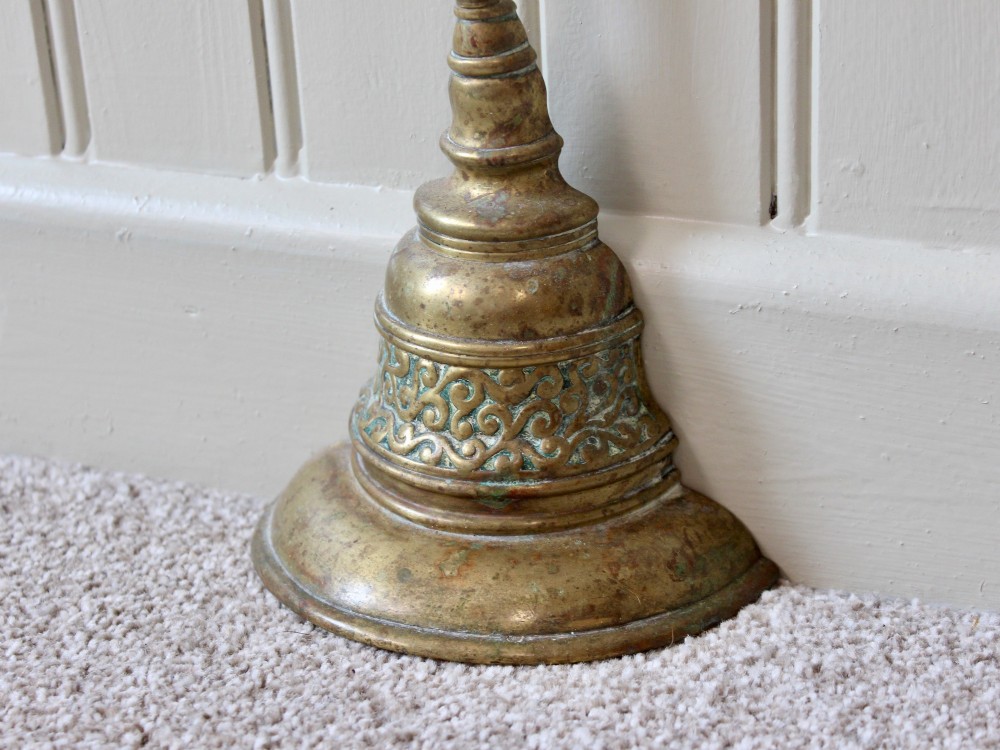 An antique Victorian cast brass door porter featuring a top loop handle, vertical stem, and weighted stepped base decorated with relief scrollwork. View III