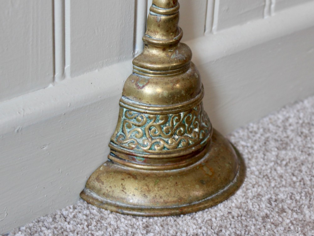 An antique Victorian cast brass door porter featuring a top loop handle, vertical stem, and weighted stepped base decorated with relief scrollwork. View IV