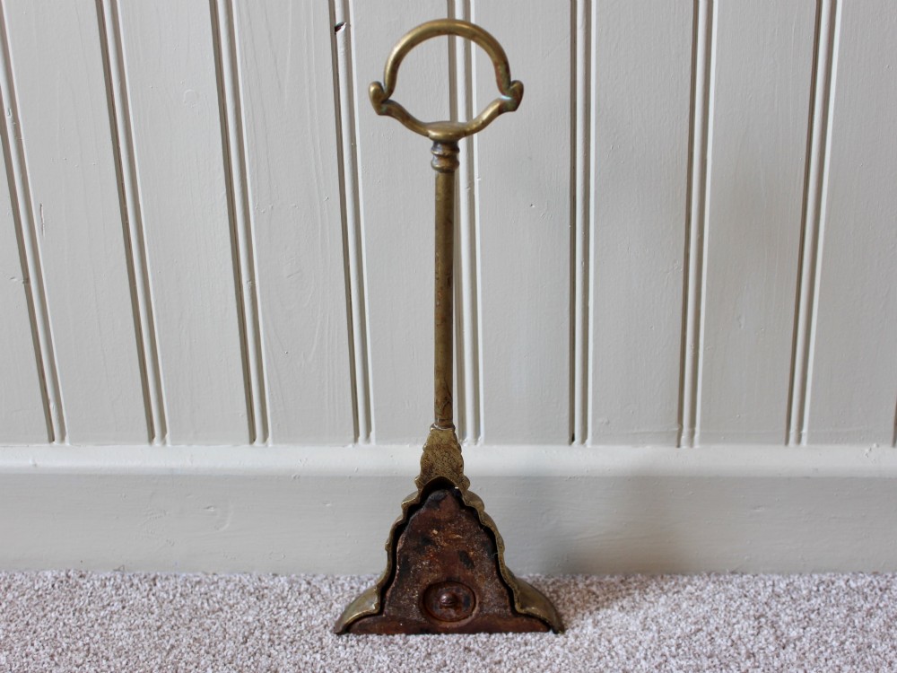 An antique Victorian cast brass door porter featuring a top loop handle, vertical stem, and weighted stepped base decorated with relief scrollwork. View V