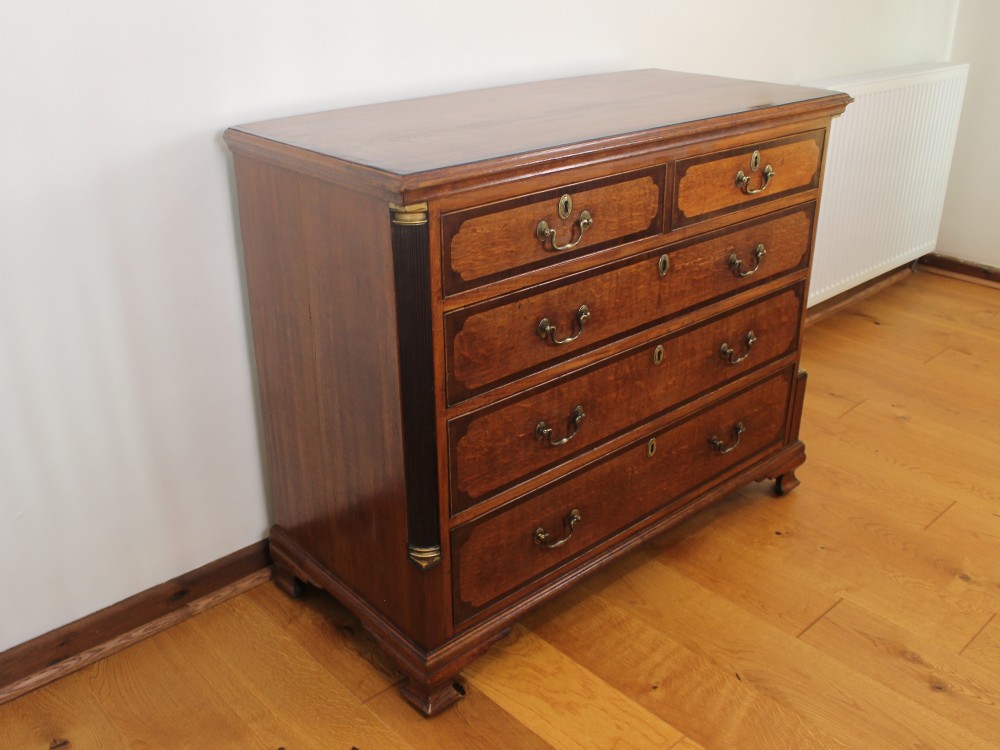 An 18th-century Georgian oak chest of drawers with mahogany crossbanding, brass handles, fluted corner columns, and bracket feet.