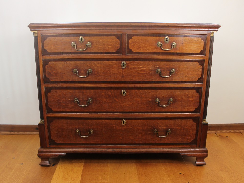 An 18th-century Georgian oak chest of drawers with mahogany crossbanding, brass handles, fluted corner columns, and bracket feet. View II