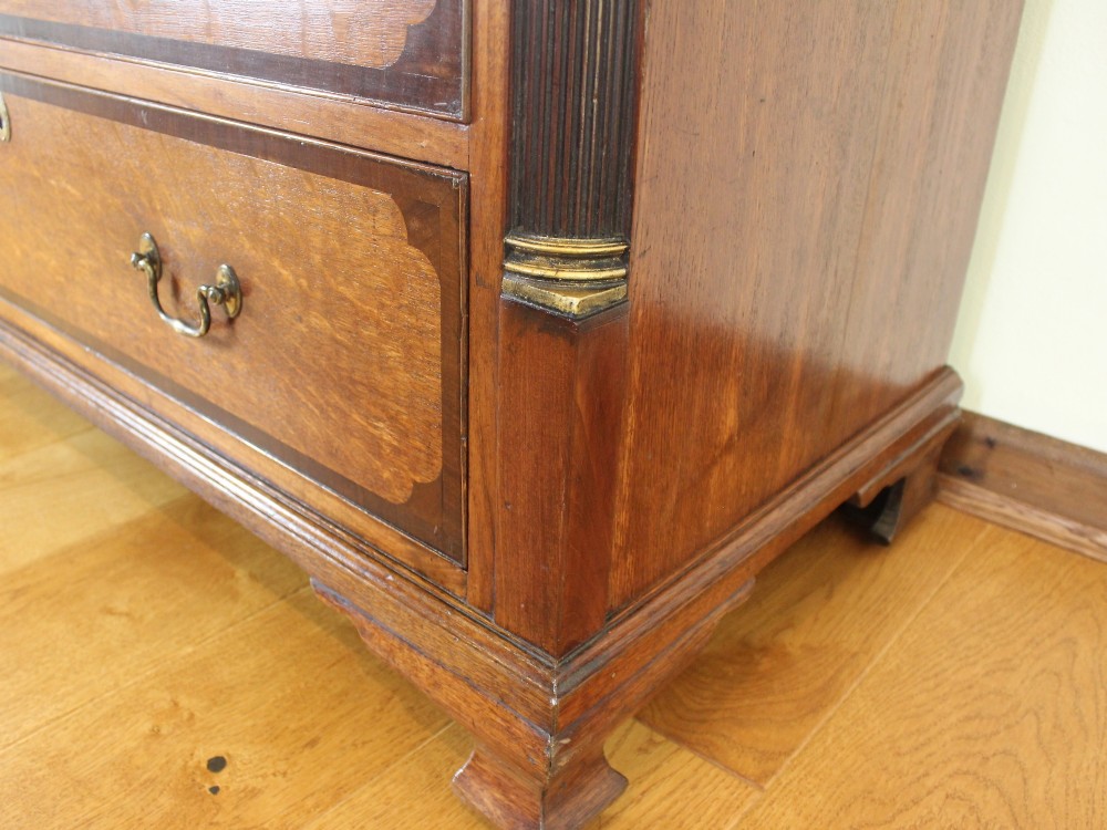 An 18th-century Georgian oak chest of drawers with mahogany crossbanding, brass handles, fluted corner columns, and bracket feet. View IX