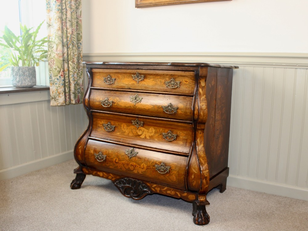 An eighteenth-century Dutch oak chest of drawers featuring a shaped bombe front, elaborate floral marquetry inlay, four graduated drawers with brass handles, and claw and ball feet.