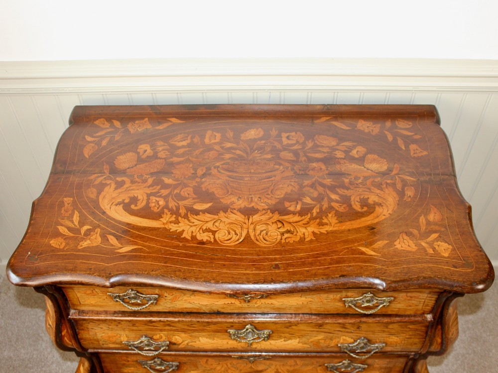 An eighteenth-century Dutch oak chest of drawers featuring a shaped bombe front, elaborate floral marquetry inlay, four graduated drawers with brass handles, and claw and ball feet. View III