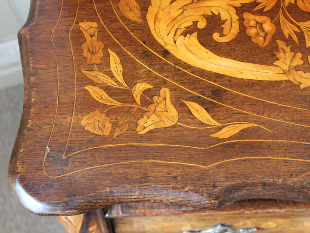 An eighteenth-century Dutch oak chest of drawers featuring a shaped bombe front, elaborate floral marquetry inlay, four graduated drawers with brass handles, and claw and ball feet. View XV