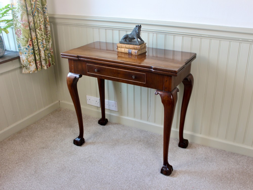 A George III mahogany fold-over card table featuring cabriole legs terminating in ball and claw feet alongside a central frieze drawer.