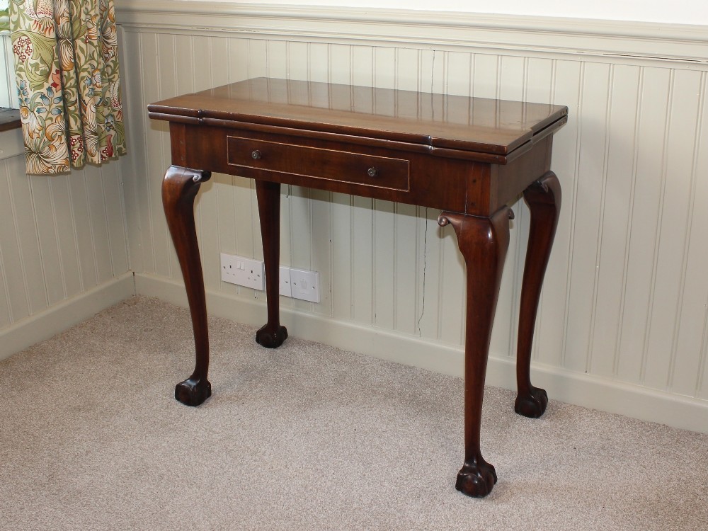 A George III mahogany fold-over card table featuring cabriole legs terminating in ball and claw feet alongside a central frieze drawer. View II