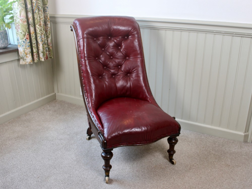 An early Victorian slipper chair featuring deep-buttoned red leather upholstery, a rosewood frame, and turned front legs on brass castors.