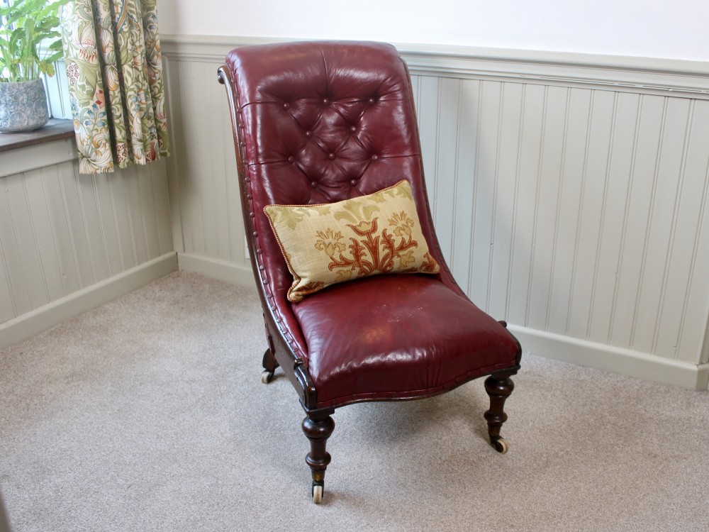 An early Victorian slipper chair featuring deep-buttoned red leather upholstery, a rosewood frame, and turned front legs on brass castors. View II