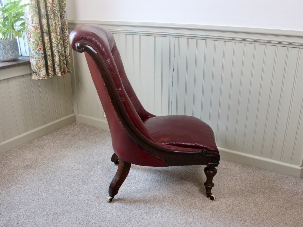 An early Victorian slipper chair featuring deep-buttoned red leather upholstery, a rosewood frame, and turned front legs on brass castors. View III
