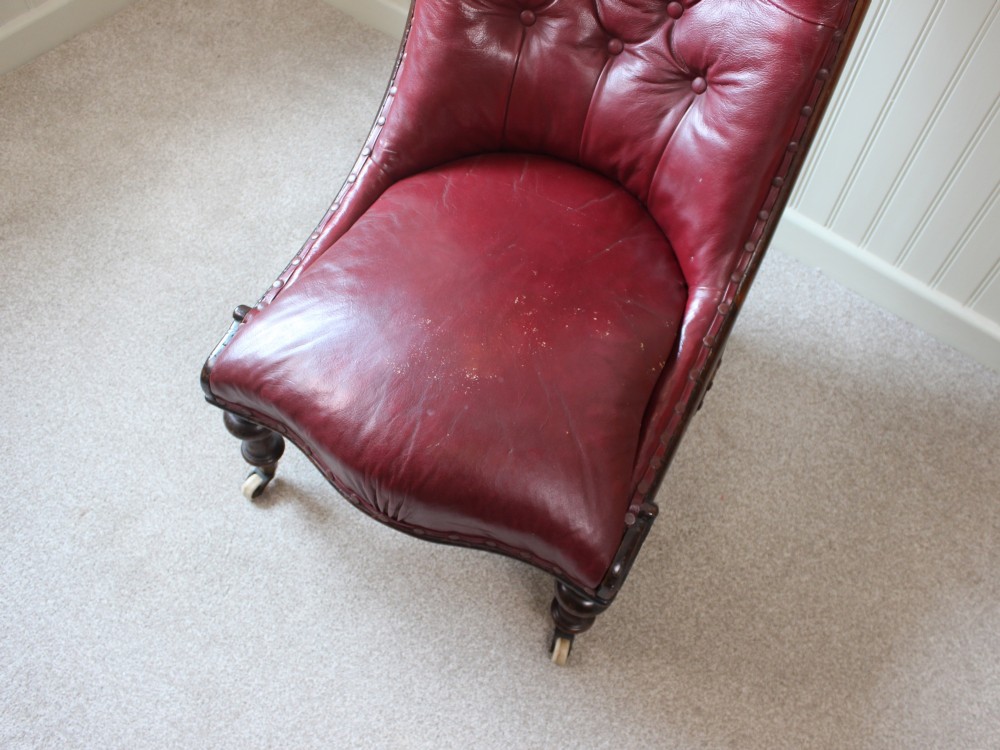 An early Victorian slipper chair featuring deep-buttoned red leather upholstery, a rosewood frame, and turned front legs on brass castors. View VIII