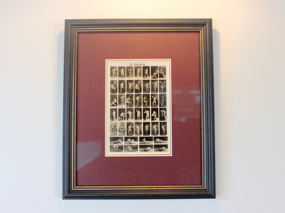 A framed 1920s monochrome photographic contact sheet displaying multiple male nude poses, mounted on burgundy card within a dark timber frame with gilt detailing.