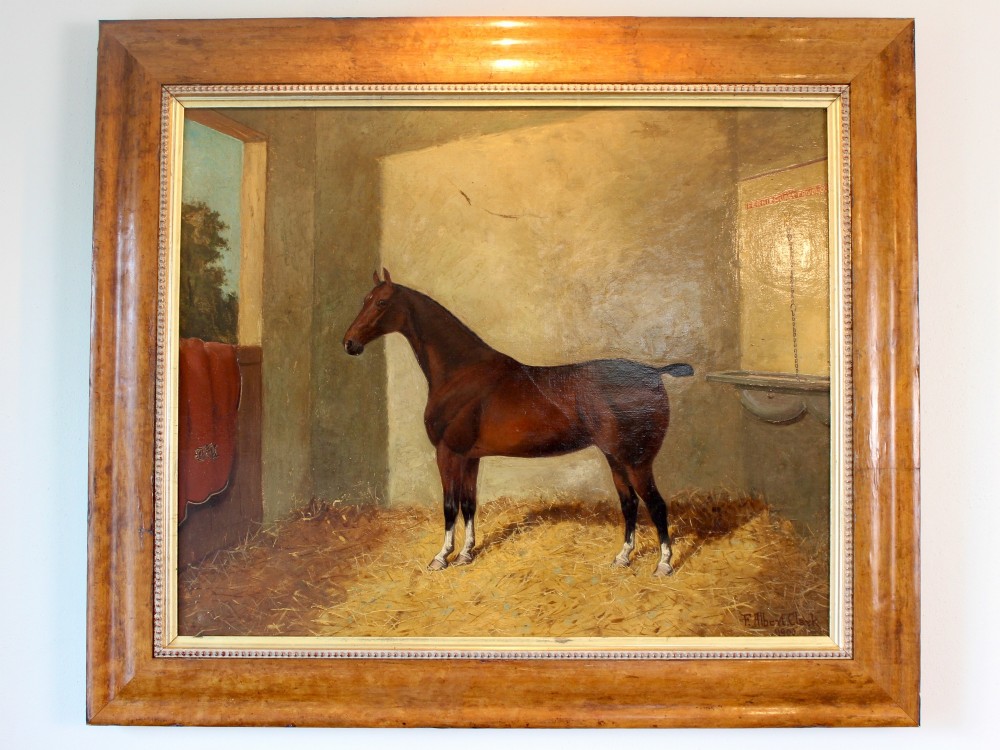 An antique oil painting depicting a bay horse standing inside a straw-filled stable within a wide timber frame. View V