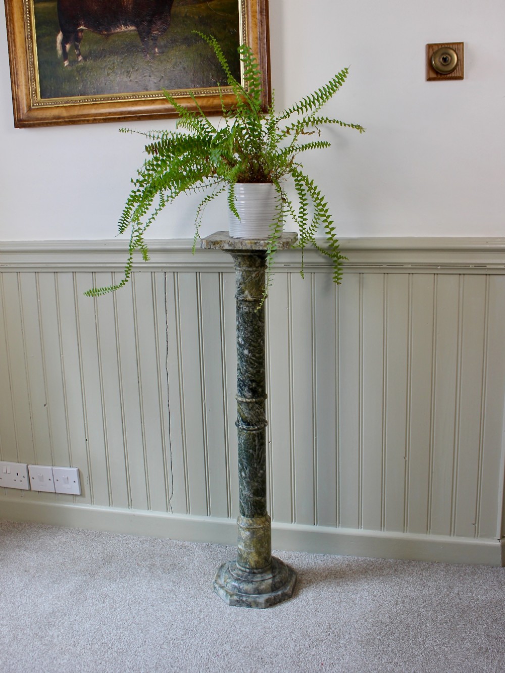 A tall Neoclassical carved green marble column pedestal featuring a square top capital, cylindrical shaft, and octagonal base.