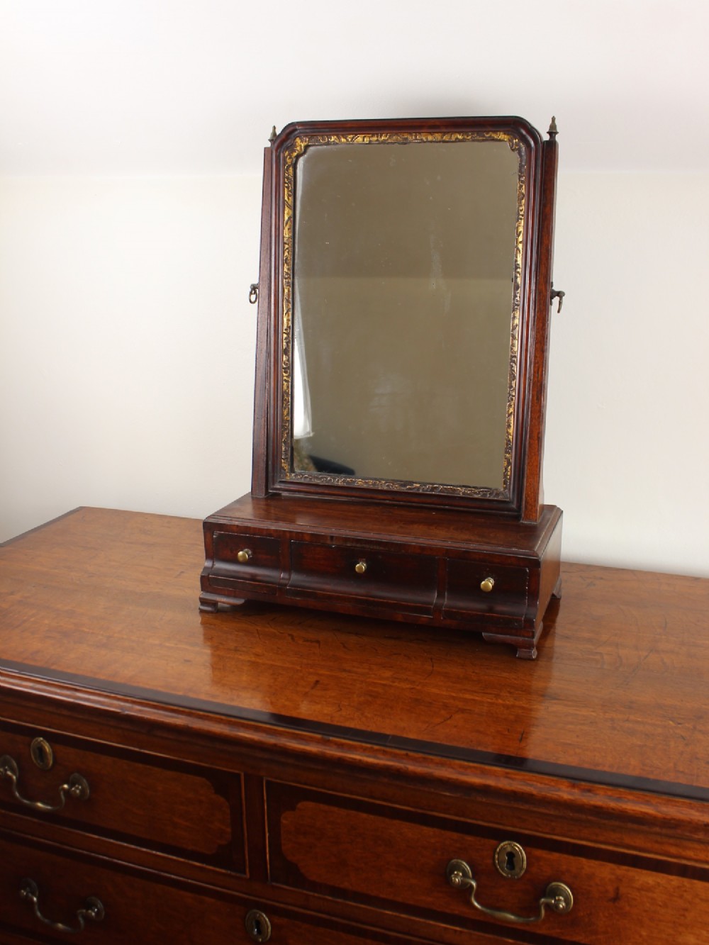 A George II mahogany dressing mirror featuring a swivel glass plate with a parcel-gilt frame resting on a three-drawer base.