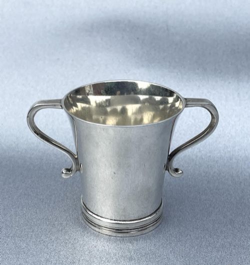 fig 1. A small George V sterling silver tot cup measure featuring twin scroll handles and visible hallmarks on the exterior body.