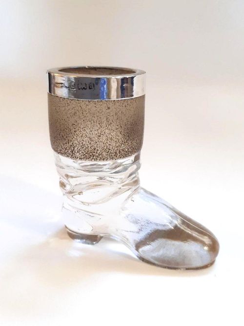 fig 1. A clear glass match striker shaped like a boot with a textured band on the collar and a polished silver rim.