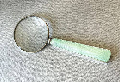 fig 1. An Art Deco magnifying glass featuring a round glass lens set in a silver frame with an elongated mint green guilloche enamel handle.