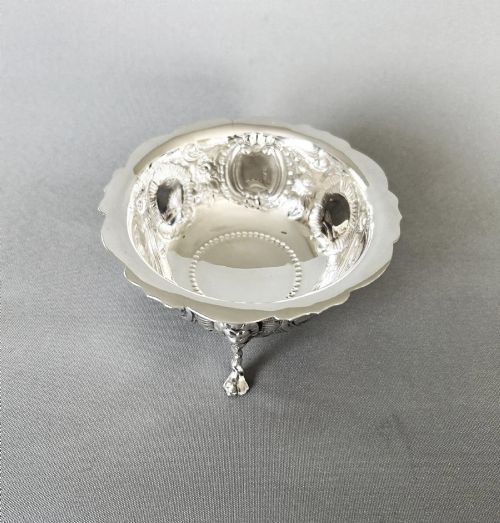 fig 1. A circular silver bowl featuring embossed goat motifs, floral repousse decoration, a scalloped rim, and three sculptural mask feet.