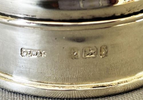 fig 1. A circular sterling silver pillbox featuring engraved scrollwork on the lid surrounding four inlaid dark green agate stones.
