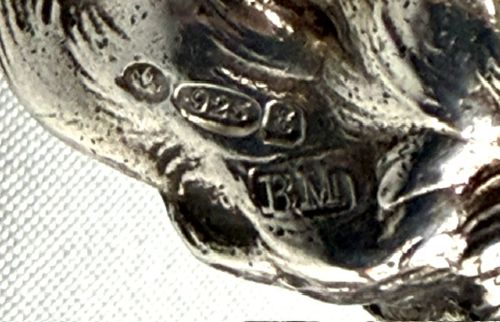 A small cast silver figure of a wolfhound standing in profile on a plain light grey surface. View III