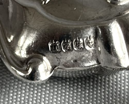 An antique sterling silver baby rattle featuring an embossed Peter Pan motif, two attached side bells, a mother-of-pearl handle, and a top mother-of-pearl teething ring. View III