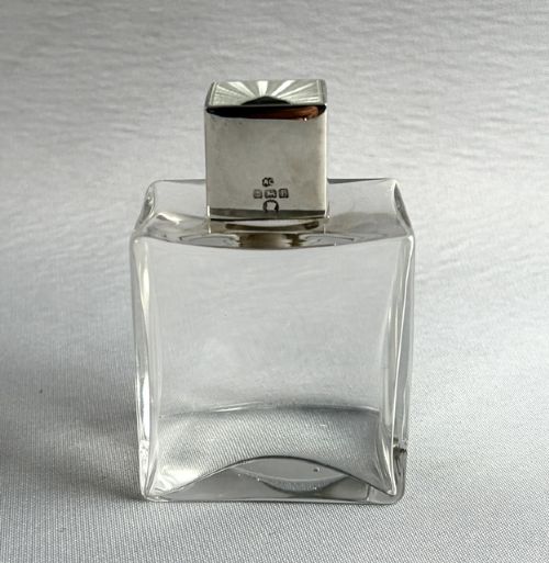 fig 1. An Art Deco clear glass cologne bottle featuring a cubic silver cap with engine-turned sunburst detailing.
