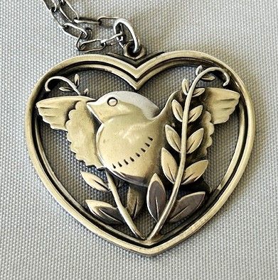 fig 1. A sterling silver heart-shaped pendant featuring a pierced bird and foliage motif suspended from a link chain.