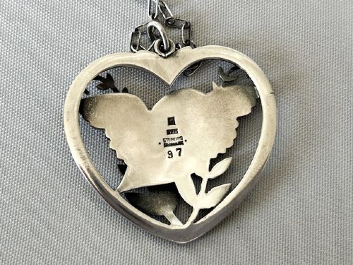 fig 2. A sterling silver heart-shaped pendant featuring a pierced bird and foliage motif suspended from a link chain.
