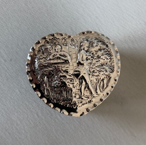 fig 1. A small Victorian silver heart-shaped trinket box featuring an embossed romantic scene on the lid and reeded vertical sides.