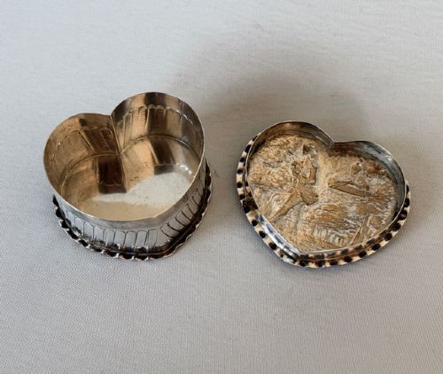 A small Victorian silver heart-shaped trinket box featuring an embossed romantic scene on the lid and reeded vertical sides. View VI