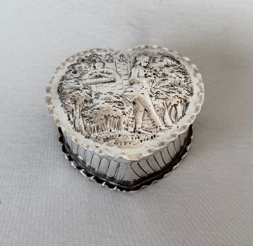 A small Victorian silver heart-shaped trinket box featuring an embossed romantic scene on the lid and reeded vertical sides. View VII