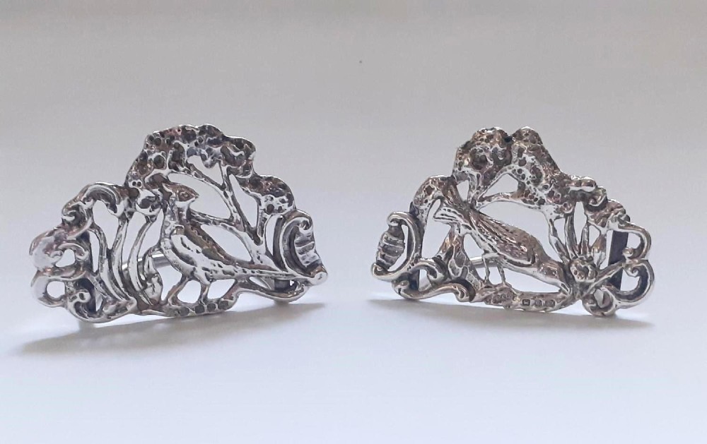 A pair of Victorian pierced sterling silver menu card holders featuring detailed bird and botanical foliage designs.