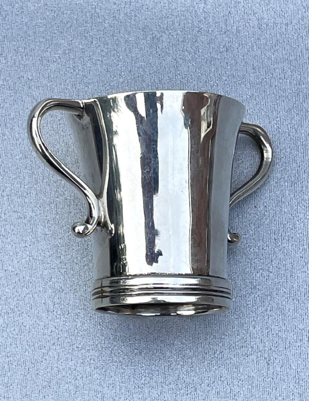 A small George V sterling silver tot cup measure featuring twin scroll handles and visible hallmarks on the exterior body. View IV