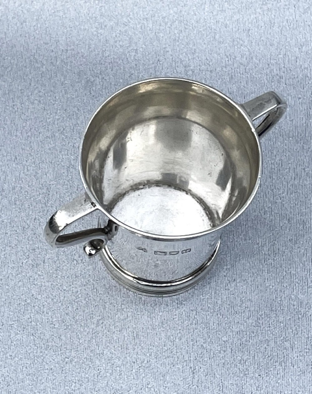 A small George V sterling silver tot cup measure featuring twin scroll handles and visible hallmarks on the exterior body. View V