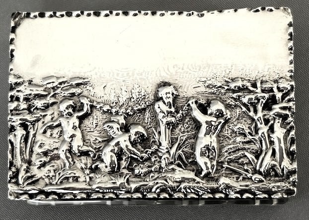 An Edwardian rectangular cut glass double stamp box featuring an embossed sterling silver lid decorated with classical cherub figures. View V