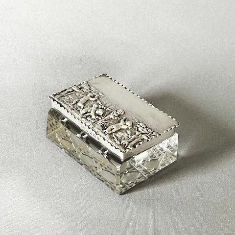 An Edwardian rectangular cut glass double stamp box featuring an embossed sterling silver lid decorated with classical cherub figures. View VII