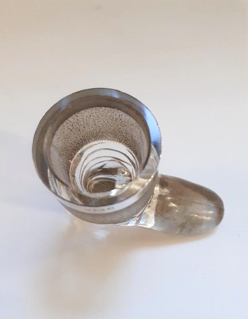 A clear glass match striker shaped like a boot with a textured band on the collar and a polished silver rim. View IV