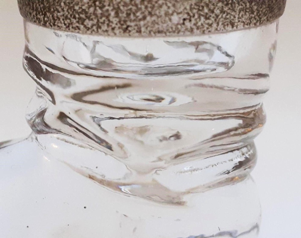 A clear glass match striker shaped like a boot with a textured band on the collar and a polished silver rim. View V