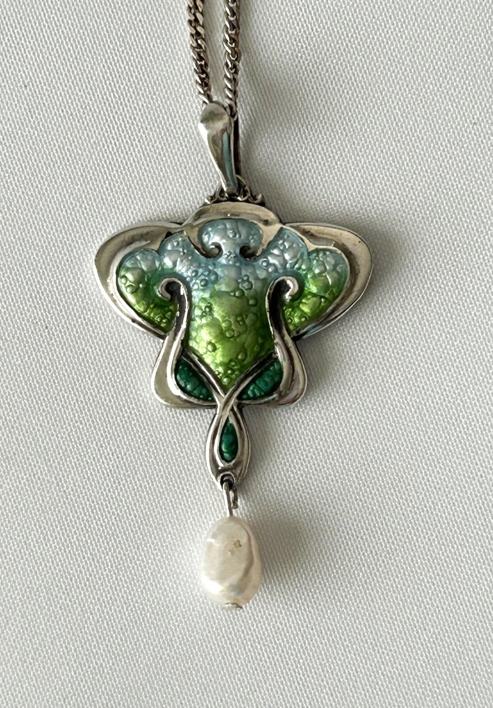 An Art Nouveau silver pendant necklace featuring green and blue enamel in an organic shape with a suspended pearl drop.
