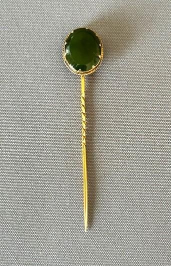 An Edwardian 9ct gold stick pin featuring an oval green jade cabochon set above a twisted gold stem.