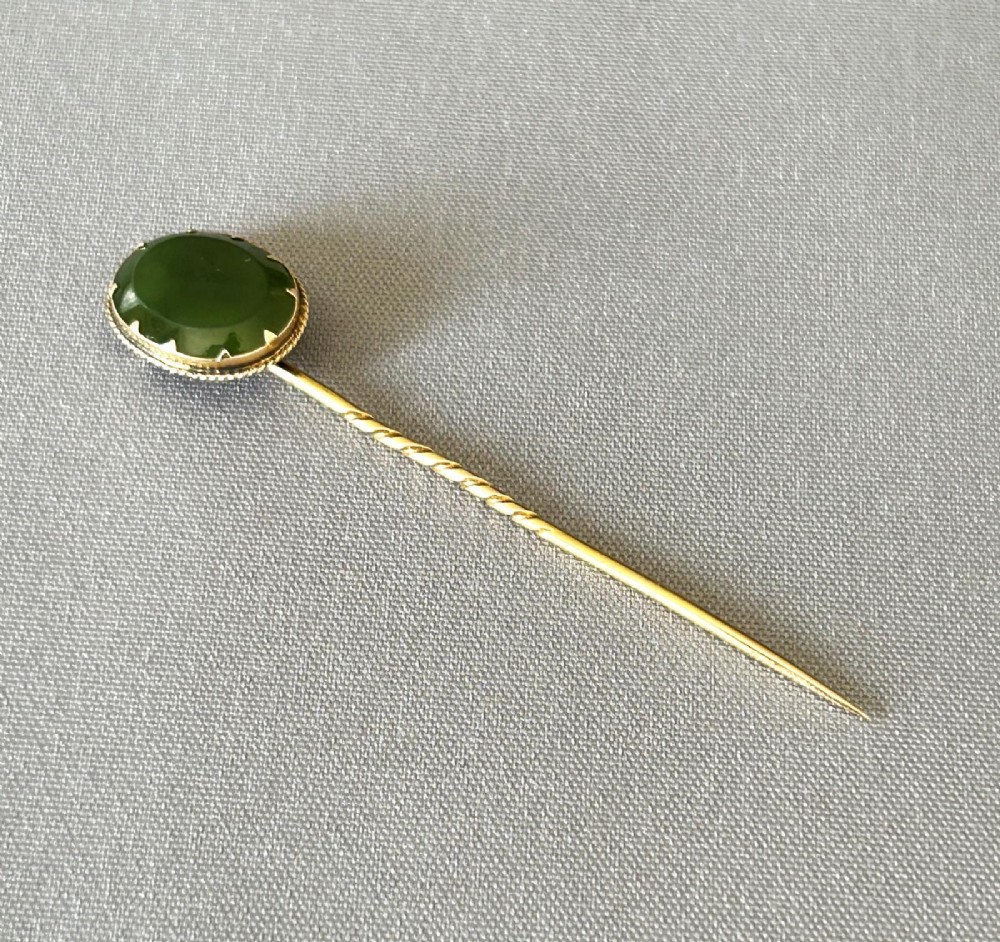 An Edwardian 9ct gold stick pin featuring an oval green jade cabochon set above a twisted gold stem. View IV